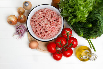 Fresh turkey mince, tomatoes, onions, garlic, herbs, cucumbers, egg, olive oil, salt and pepper on a table