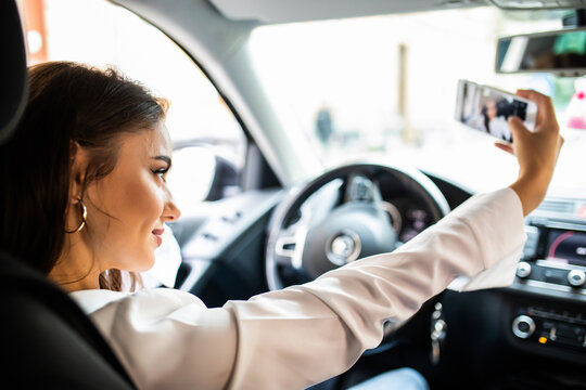 Smiling young woman taking selfie picture with smart phone in car