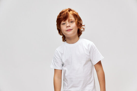 Cheerful red-haired boy in white t-shirt gray background 