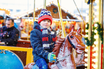 Fototapeta na wymiar Adorable little kid boy riding on a merry go round carousel horse at Christmas funfair or market, outdoors. Happy child having fun on traditional family xmas market in Germany