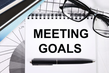MEETING GOALS. TEXT ON WHITE PAPER. NEAR FINANCIAL CHARTS AND POINTS. VIEW FROM ABOVE. CLOSE-UP. CAPITAL LETTERS BUSINESS CONCEPT