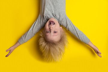 Happy blond boy hanging upside down with arms outstretched. Child on bright yellow background © somemeans