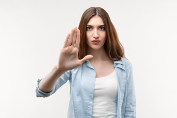 Serious girl with long chestnut hair, dressed in casual clothes shows a stop with her hand, showing symbol of rejection, not allow violence, body language. Human emotions, facial expression concept.