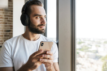 Image of unshaven focused man using headphones and mobile phone
