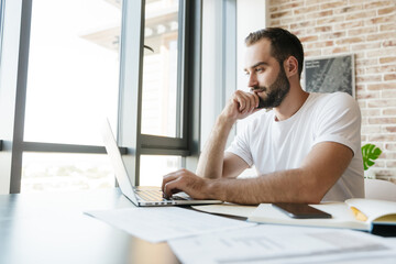 Fototapeta premium Image of young man working with laptop while sitting at table