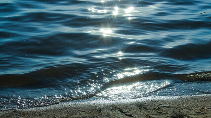Sun glare in waves of sea water on a tropical beach in summer in nature close-up. Beautiful texture of water waves.Sea wave and sand seashore. Golden sun light over the sea ocean waves. 
