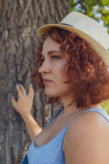 red-haired curly-haired girl in a summer braided headgear and jeans dress posing in the village ....