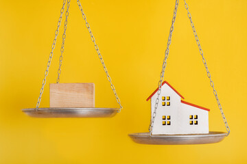 Balance scales and model home. Yellow background, close up. Choice concept.