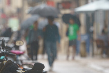 Defocused photography of people at the city street in the rainy summer day. Lifestyle of big city Bordeaux. The street of downtown is full of people even in the rain. Umbrellas everywhere. 