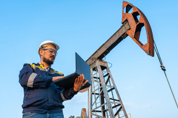Engineer with a laptop against the background of oil rockers.