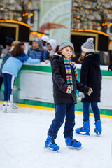 Two happy little kids girl and boy in colorful warm clothes skating on a rink of Christmas market or fair. Healthy children having fun on ice skate. Lot of people having active winter leisure.