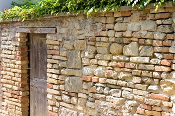 Isolated wooden door in a brick wall with plants on the roof (Fiorenzuola di Focara, Pesaro, Italy,...