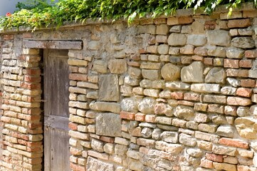 Isolated wooden door in a brick wall with plants on the roof (Fiorenzuola di Focara, Pesaro, Italy, Europe)