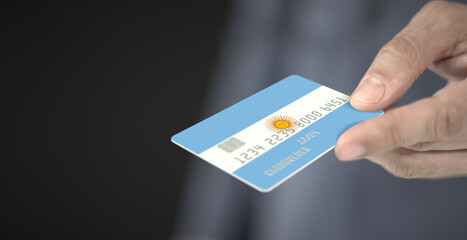 Man gives credit card with printed flag of Argentina, close-up shot. Fictional numbers