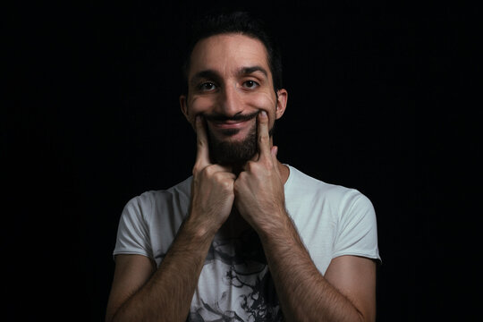 put on a smile with your fingers. The guy shows a fake smile. Photo on a black background.