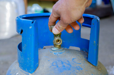 Caucasian man opening the valve on blue propan butan gas tank.