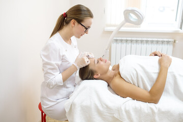 Obraz premium The beautician makes the patient injections and the forehead area during the procedure of mesotherapy and botox