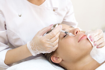 The beautician makes the patient augmentation of the lips with the help of injections of the hyaluronic acid filler