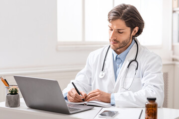 Focused watching webinar on laptop and taking notes at office