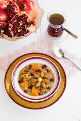 Traditional Turkish Dessert Ashure or Noah's Pudding designed flower shape in white bowl,on white surface with fresh pomegranate and tea.