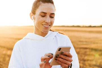 Image of smiling sportswoman using mobile phone while working out
