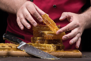 The chef serves bee honey in combs with his hands. Close up on a wooden table. Organic farm food concept.