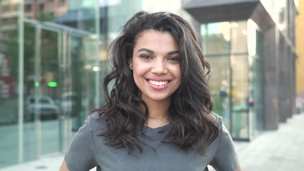 Happy stylish young mixed race gen z girl wearing tshirt standing on city street looking at camera, portrait. Pretty millennial Afro American ethnic woman dental smile closeup outdoor face headshot.