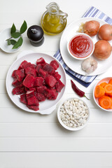 Raw beef, white beans, onions, carrots, garlic, bay leaf, pepper, tomato paste and olive oil on a white table