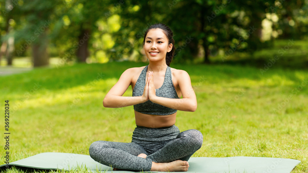 Wall mural calm asian girl meditating in lotus pose during her yoga class outdoors