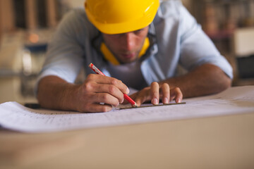 Young carpenter underlining blueprint using pencil and a ruler