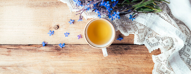 wooden background with a bouquet of blue flowers and a cup of tea. long banner