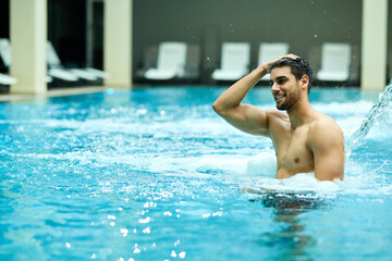 Young happy man enjoying in a swimming pool at health spa.