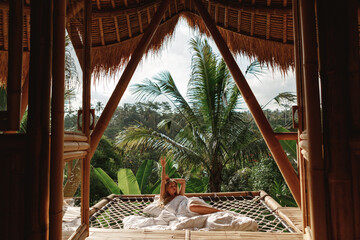 The woman on the hammock in the morning in the wooden bamboo house, enjoy tropical vacation on Bali...