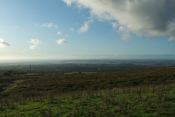 Obraz premium View from the foothills of the Snowdonia mountains to the sea and the beautiful Welsh island of Anglesey. Hillside with gorse and heather. Lush coastal plain in the distance. Blue sky – copy space.