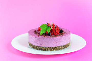 Raw cashew black currant cake on a chocolate granola, garnished with fresh berries on a pink background. Sugar, lactose, gluten free.