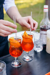 The bartender inserts straws into orange cocktails. Aperol spritz in a glass tulip. Summer party catering. No face.
