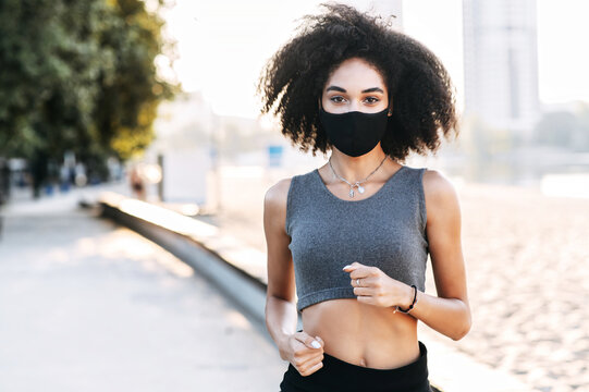 Sports training outdoor in safety during epidemic, quarantine. An African-American woman jogs with a medical mask on the face. Close-up portrait, copy space
