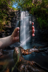 Hand holding smart phone. Pop Up 3d. a small waterfall and its river crosses the phone screen to follow its course