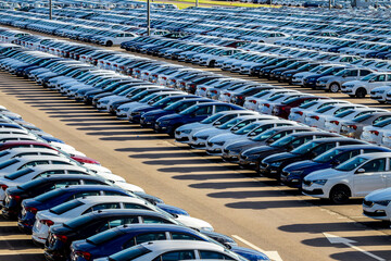 Rows of a new cars parked in a distribution center on a car factory on a sunny day. Top view to the parking in the open air. © Eugene_Photo