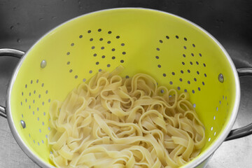 Boiled tagliatelle pasta straining in a colander in a metal sink
