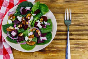 Tasty spinach salad with boiled beetroot, feta cheese, walnut and red onion on wooden table. Top view. Healthy vegetarian food