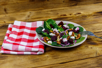 Tasty spinach salad with boiled beetroot, feta cheese, walnut and red onion on wooden table. Healthy vegetarian food