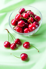 Juicy ripe sweet cherries in glass bowl on gently green cloth background