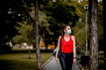 Naklejka premium Young Caucasian woman with protective face mask on her way to training in a public park.