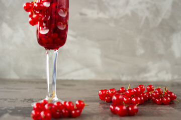 Red currant in a shot glass, the rest is scattered around it on a gray textured background
