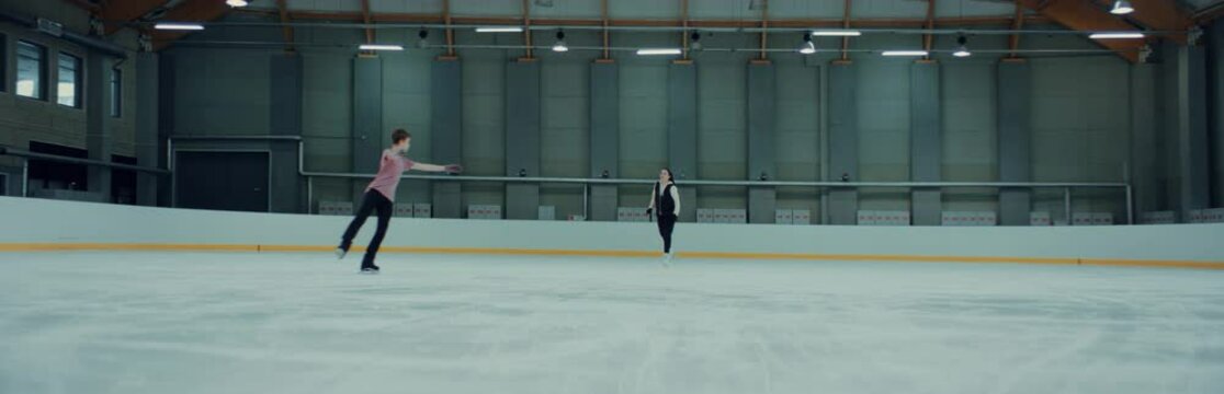 Professional teenager figure skater parcticing with his trainer on ice. Shot on RED cinema camera with 2x Anamorphic lens, 75 FPS Slow motion