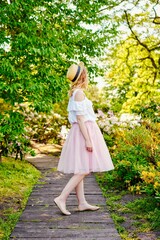 Gorgeous young  woman in hat posing in a blooming garden. Beautiful girl dressed in pink skirt and white blouse. Sensual woman with perfect skin and with natural makeup. fashion and style concept.