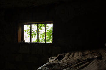 Light enters a dark barn through a small window in which a green tree is visible.