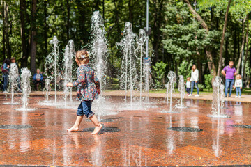 Kyiv (Kiev), Ukraine - July 31, 2020: A little pretty girl is enjoying time, having fun, running and playing in a park near a big fountain with many splashes