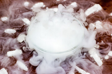 White cool dry ice (frozen carbon dioxide) with smoke effect in the glass bowl on the dark brown wooden background.